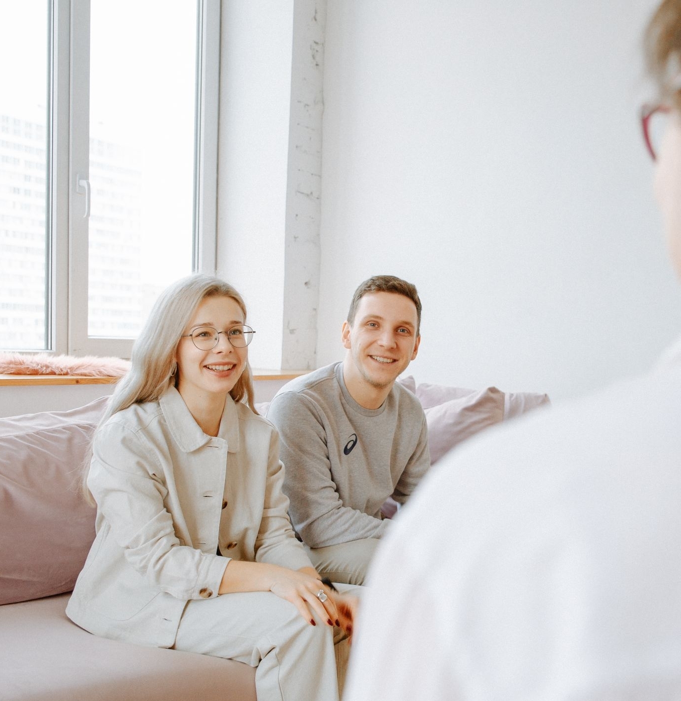 A couple smiles while sitting on a sofa during a counseling session indoors.
