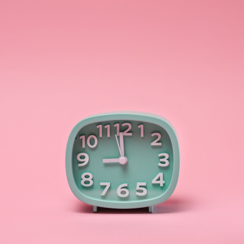 Minimalist pastel green analog clock set against a pink backdrop with copy space.